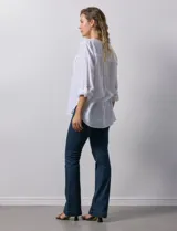 Blusa blanca de lino y rayón, con cuello a la base, escote en V y abertura con botones. Tiene bolsillos en la parte delantera y mangas largas regulables con presilla y botón.