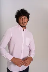Camisa de manga larga confeccionada en tejido poplin con diseño de rayas verticales finas en color rosado y blanco. Presenta cuello abotonado (button-down), cierre frontal con botones y un bolsillo en el pecho.