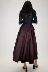 Falda midi asimétrica de color bordó, confeccionada en tejido satinado con volumen. Presenta un diseño con volados en la cintura y cierre de cremallera oculta en la espalda.