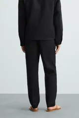 Pantalón negro de corte regular fit, confeccionado en tejido de lino. Presenta cintura con botón y cierre de cremallera, bolsillos frontales y bolsillos traseros de doble vivo.