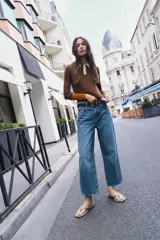 Jeans blancos wide leg cropped de tiro alto, con diseño de cinco bolsillos y pernera ancha y corta. Incluye un cinturón fino de color marrón oscuro con hebilla metálica y cuenta con cierre frontal de cremallera y botón metálico.