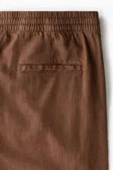 Pantalón de corte relajado color marrón, confeccionado en mezcla de lino y viscosa, con cintura elástica ajustable mediante cordón y bolsillos laterales.