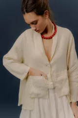 Chaqueta de lino color beige, de calce relajado, con escote en V, cierre frontal con botones y bolsillos frontales aplicados.