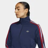 Campera azul marino de tricot con cierre frontal, cuello alto y corte clásico. Presenta las tres líneas características de Adidas en rojo y blanco a lo largo de las mangas y el logo dorado bordado en el pecho.