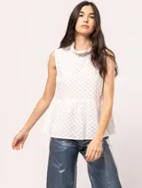Blusa blanca sin mangas, con cuello alto con volados y detalles bordados con motivos florales.