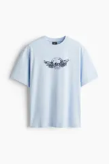 Remera celeste de corte holgado, con cuello redondo y diseño estampado en el pecho con texto y alas.