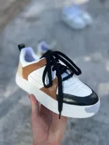 Zapatillas urbanas de cuero sintético color blanco, con puntera y talón en negro, laterales en marrón y cordones negros.