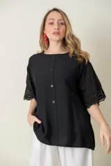 Blusa negra de viscosa con mangas cortas y detalle de broderie en los puños. Tiene cuello redondo y cierre frontal con botones.