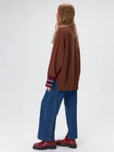 Pullover de punto color rojo, con cuello tortuga, corte holgado y mangas largas con puños acanalados en contraste con rayas blancas. Presenta un logo bordado en el pecho.