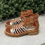 Sandalias bajas de cuero color beige con tiras horizontales plateadas y cierre con hebilla al tobillo.