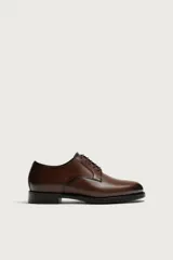 Zapato de vestir estilo Derby en piel color marrón oscuro, con cordones del mismo tono, horma redonda y suela con ligero tacón.