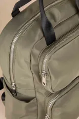 Mochila color verde militar de nylon con asa fija doble, dos bolsillos externos frontales con cierre, dos compartimentos laterales y un compartimento interno grande.