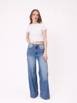 Jean de corte wide leg con diseño de pata ancha y costuras laterales decorativas. Presenta un lavado azul medio con efecto desgastado y ruedo desflecado.