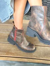 Botas cortas de cuero color chocolate, con elástico lateral, cierre interno con cremallera roja, pespuntes rojos y suela track.