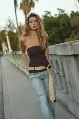 Top palabra de honor color marrón oscuro, con escote recto y hombros descubiertos. Incluye un cinturón en forma de corbata con estampado geométrico en tonos beige y blanco, que se anuda en la parte frontal. Cierre lateral con cremallera oculta.