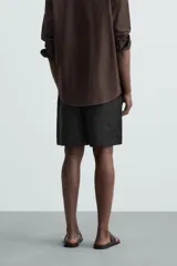 Bermuda de lino color blanco hueso, de corte relajado y tiro medio. Presenta cintura elástica ajustable con cordón, pliegues frontales y bolsillos laterales y trasero.