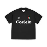 Camiseta de fútbol de manga corta en color negro, con cuello en V. Presenta el logo de la marca Corteiz en el pecho, junto a un escudo con los colores de la bandera italiana y una estrella dorada. El nombre de la marca aparece estampado en grande en el centro del frente.