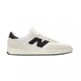 Championes urbanos New Balance modelo 440, de diseño bajo con combinación de colores blanco y crema. Presenta el logo 'N' en color negro en los laterales, refuerzos de gamuza en la puntera y talón, y perforaciones decorativas en la parte trasera.