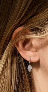 Aros abridores de acero plateado con diseño de argolla y dije colgante en forma de mano de Fátima (Hamsa), completamente pavimentados con circones brillantes.