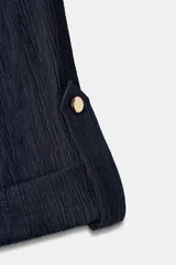 Camisa estilo safari de color azul marino con textura efecto arrugado, cuello solapa, mangas remangadas y cierre frontal con botones. Presenta bolsillos delanteros con solapa y un cinturón fino ajustable en la cintura.