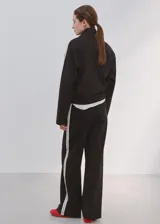 Pantalón deportivo negro con líneas blancas laterales, tiro alto y diseño recto.