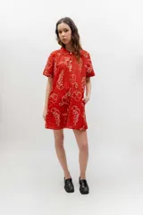 Vestido corto de lino y algodón color rojo, con estampado de cuadros y flores en tono blanco. Cuenta con cuello redondo, cierre frontal con botones y mangas cortas.