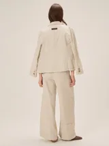 Pantalón sastrero de corte ancho, color beige con rayas verticales blancas y detalles de costuras pespunteadas.