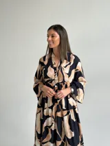 Vestido largo negro con estampado de hojas en tonos beige y tostado, de corte amplio y fluido, con escote en V y botonadura frontal parcial. Cuenta con mangas largas y volados en el faldón.