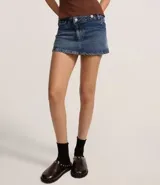 Minifalda de jeans azul oscuro, con cintura alta y cierre cruzado con botones. Presenta trabillas y bolsillos delanteros y traseros.