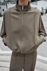 Cazadora estilo bomber color gris, con cuello subido, manga larga, bolsillos delanteros de vivo y cierre frontal con cremallera. Presenta bajo ajustable con cordones elásticos laterales.