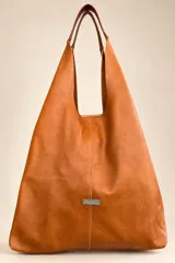 Bolso tipo tote de cuero color tostado, de gran capacidad, con asas de hombro y placa metálica con el logo de la marca en la parte frontal.