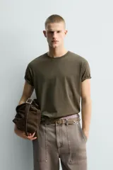 Camiseta de algodón color verde oliva, corte regular fit, con cuello redondo y manga corta. Presenta un pequeño corazón bordado en la manga.