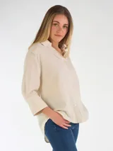 Camisa oversize de lino color beige, con cuello clásico, cierre frontal con botones y mangas largas con puños anchos.