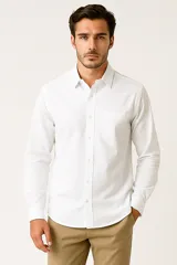 Camisa de lino de manga larga, color blanco, con cuello clásico y cierre frontal de botones. Presenta un bolsillo frontal en el pecho.