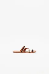 Sandalia chata de cuero vacuno con diseño de tiras finas multicolores y anillo para el dedo. Presenta tiras en color negro, dorado con acabado brillante, plateado metalizado y beige sobre una suela plana de cuero marrón.