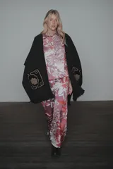 Ruana de tejido de punto color negro, con diseño abierto, flecos en el ruedo y bolsillos frontales destacados con bordados artesanales en tonos contrastantes.