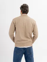 Campera tejida de punto en color beige, con diseño de trenzas y rombos, cuello alto y cierre frontal completo.
