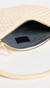 Bandolera color crema, tejida a mano, con correa al hombro de cuero color beige y cierre superior con cremallera.