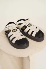 Sandalias de tiras anchas color crema con ajuste de hebilla al tobillo y suela track negra.