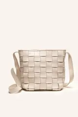 Cartera tipo morral de cuero color beige, con diseño trenzado artesanal, correa larga regulable y cierre superior.