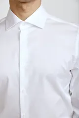 Camisa de vestir blanca de corte clásico, con cuello rígido, cierre frontal de botones y mangas largas con puños abotonados.
