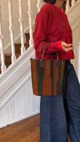 Matera de cuero con diseño de paneles verticales en combinación de colores azul, verde, marrón y bordó. Cuenta con dos asas cortas de cuero y estructura rígida.