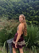 Vestido corto de tela metalizada en tono fucsia con reflejos dorados, con escote en V, diseño de top con triángulos, aberturas laterales en la cintura y doble volado irregular en el ruedo.