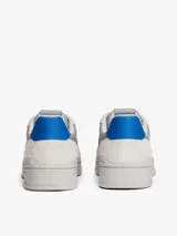 Zapatillas Tommy Jeans de corte bajo, confeccionadas en ante con paneles de malla y cuero sintético. Presentan un diseño en tonos gris y blanco con detalles en azul vibrante, cordones moteados y suela cupsole de goma con logo en bajo relieve.