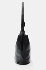 Bolso tipo saca de diseño asimétrico confeccionado en piel negra con acabado brillante. Cuenta con asa de hombro ajustable y cierre mediante imán. Incluye un bolsillo extraíble en su interior.