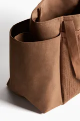 Cartera shopper grande en tejido grueso de mezcla de yute color marrón, con compartimento de malla en el frente y doble asa superior.