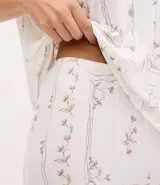 Pijama de dos piezas compuesto por una blusa de manga corta con escote en V decorado con encaje y un pantalón estilo capri con cintura elástica y terminaciones de encaje en el ruedo. Presenta un estampado floral delicado sobre fondo claro.