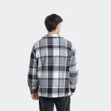 Camisa de franela a cuadros en tonos grises, blancos y negros, forrada con corderito sintético en el interior. Cuenta con mangas largas, bolsillos con solapa en el pecho y cierre frontal con botones.