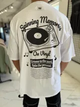 Remera oversize blanca de manga corta, con gran estampado en la espalda de una bandeja de vinilos y texto temático musical.