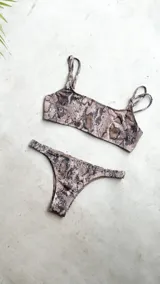 Conjunto de bikini con corpiño estilo bandó alto y breteles regulables, con lazo para atar en la espalda. La bombacha es vedetina con frunce elástico en los costados. Presenta un estampado tipo tie-dye o marmolado en tonos azules y naranjas/terracota.
